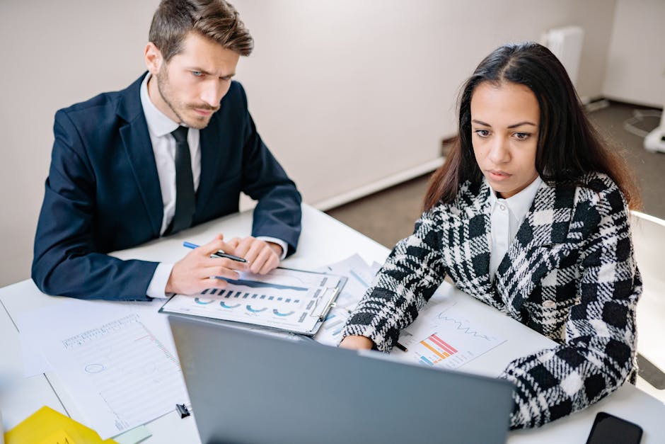 A man and woman collaborate on business analysis at a desk with charts in an office setting