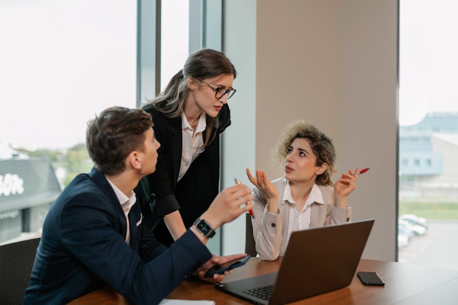 Three professionals in a business meeting, discussing work around a laptop in a modern office