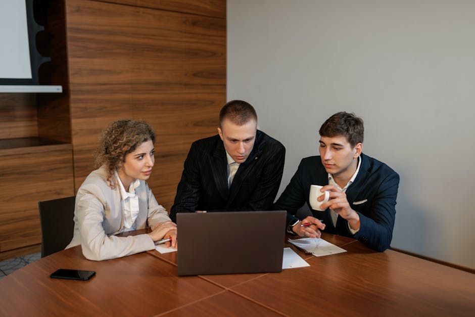 Three professionals collaborate in a modern office setting focused on a laptop
