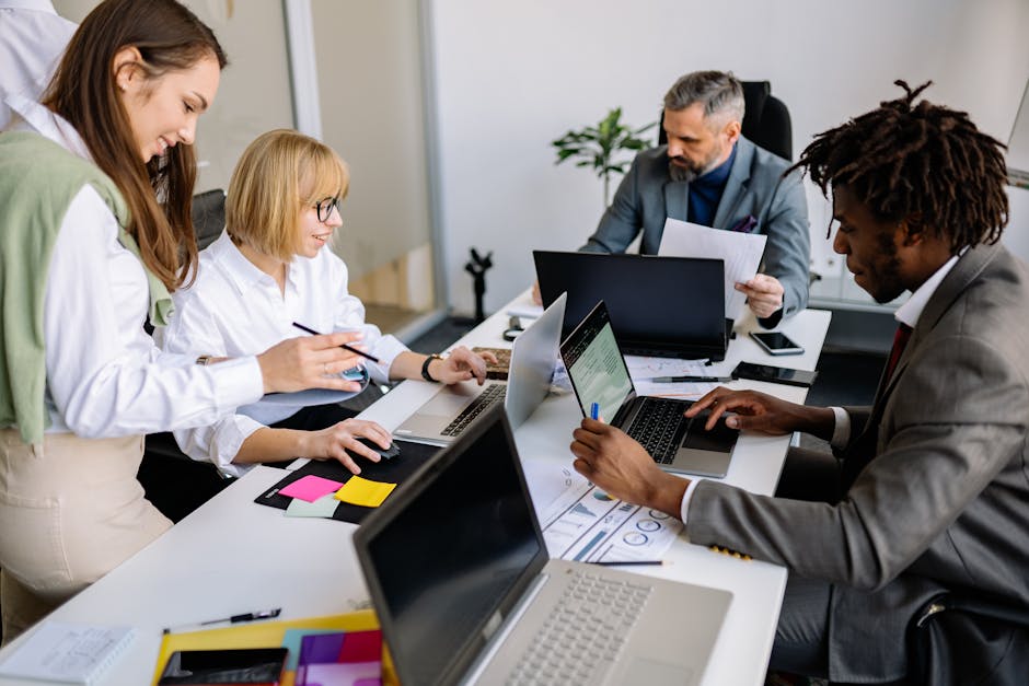 A diverse team collaborates in a modern office setting with laptops and documents